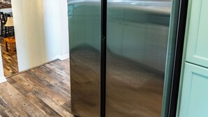 Uma geladeira de aço inoxidável em uma cozinha com piso de madeira e paredes claras.