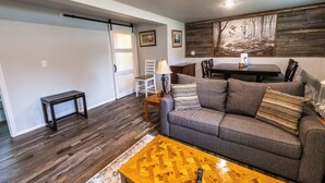 Uma sala de estar com sofá cinza, mesa de centro de madeira e um quadro na parede.