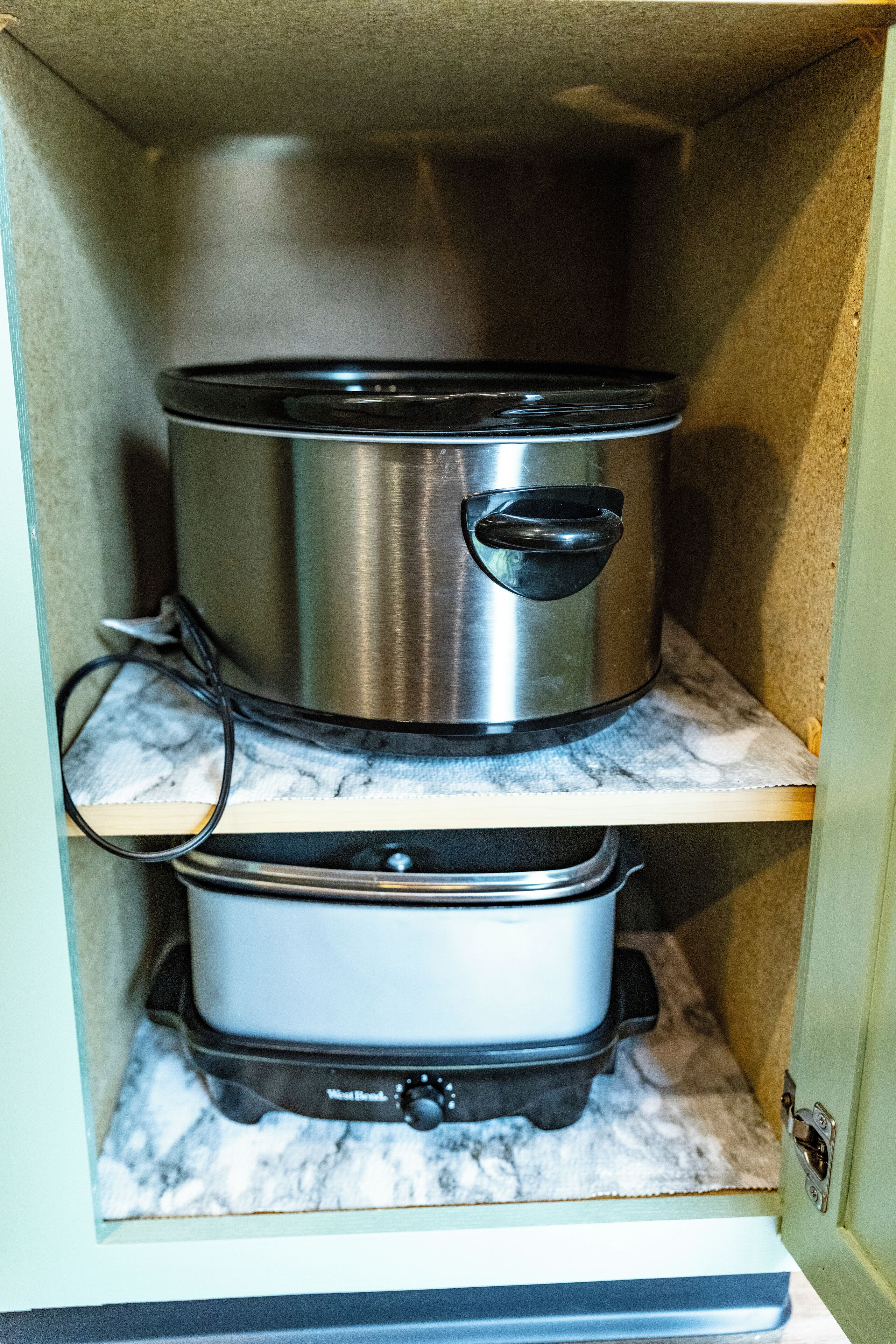 A kitchen cabinet with two stainless steel pots on marble shelves.