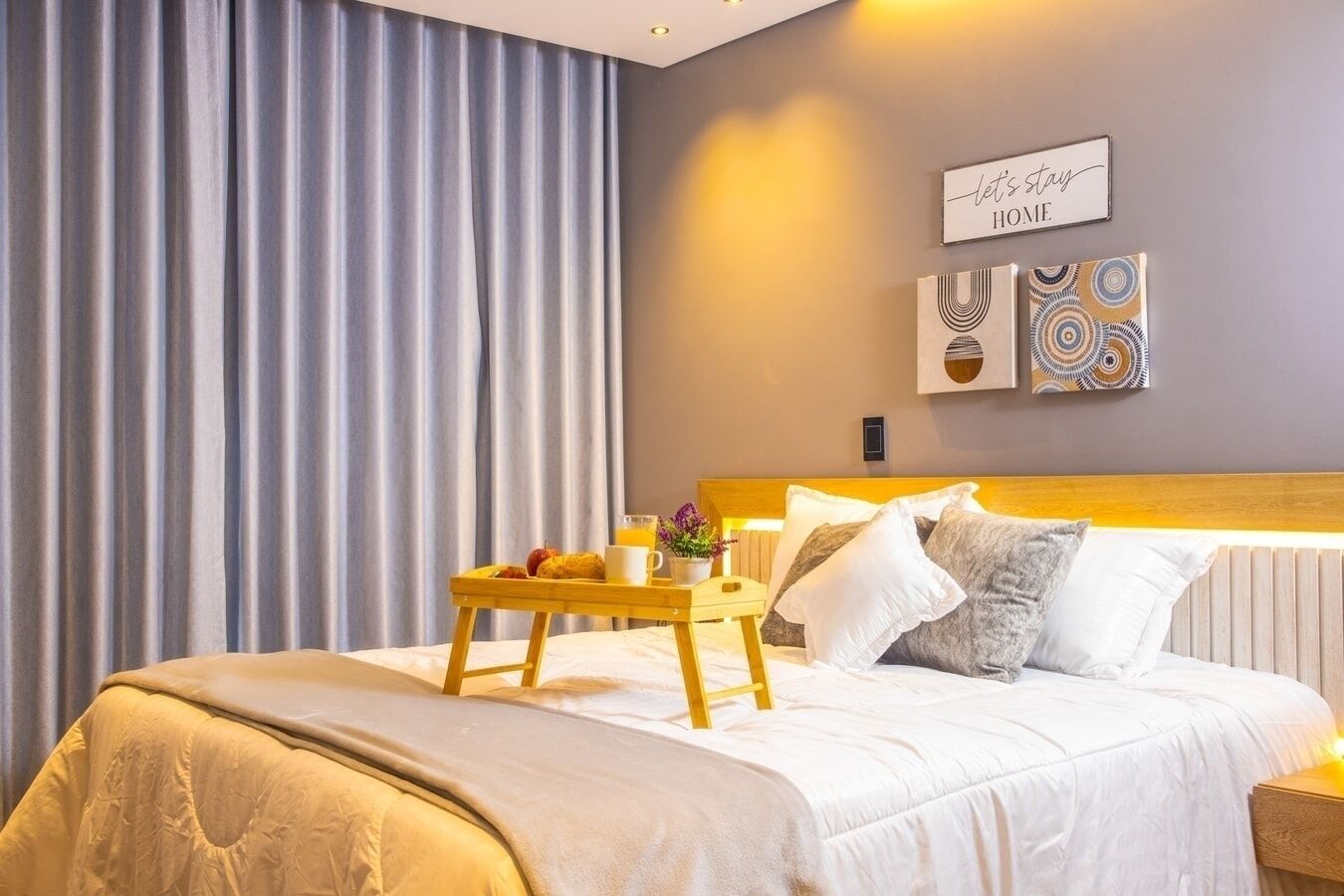Una habitación de hotel con una cama, una mesita de noche, una bandeja con alimentos para el desayuno y una pared decorada.