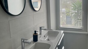 Ein modernes Badezimmer mit zwei Waschbecken, einem Spiegel und einem Fenster mit Jalousien.