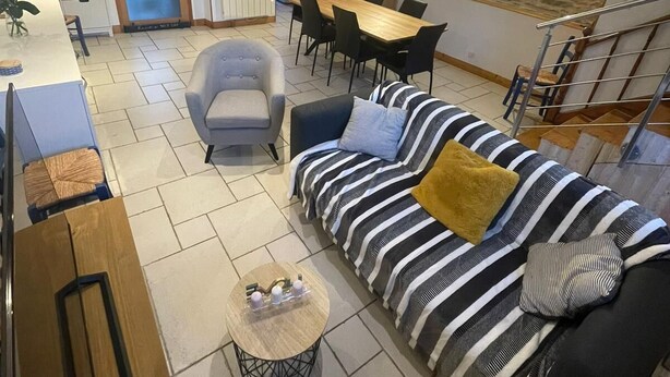 Ein großzügiger Wohnbereich mit Sofa, Sessel und Esstisch. Im Hintergrund ist eine Treppe zu sehen.