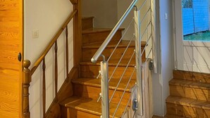 Eine Holztreppe mit Metallgeländer, ein kleines Fenster oben und eine Tür, die zu einem Außenbereich führt.