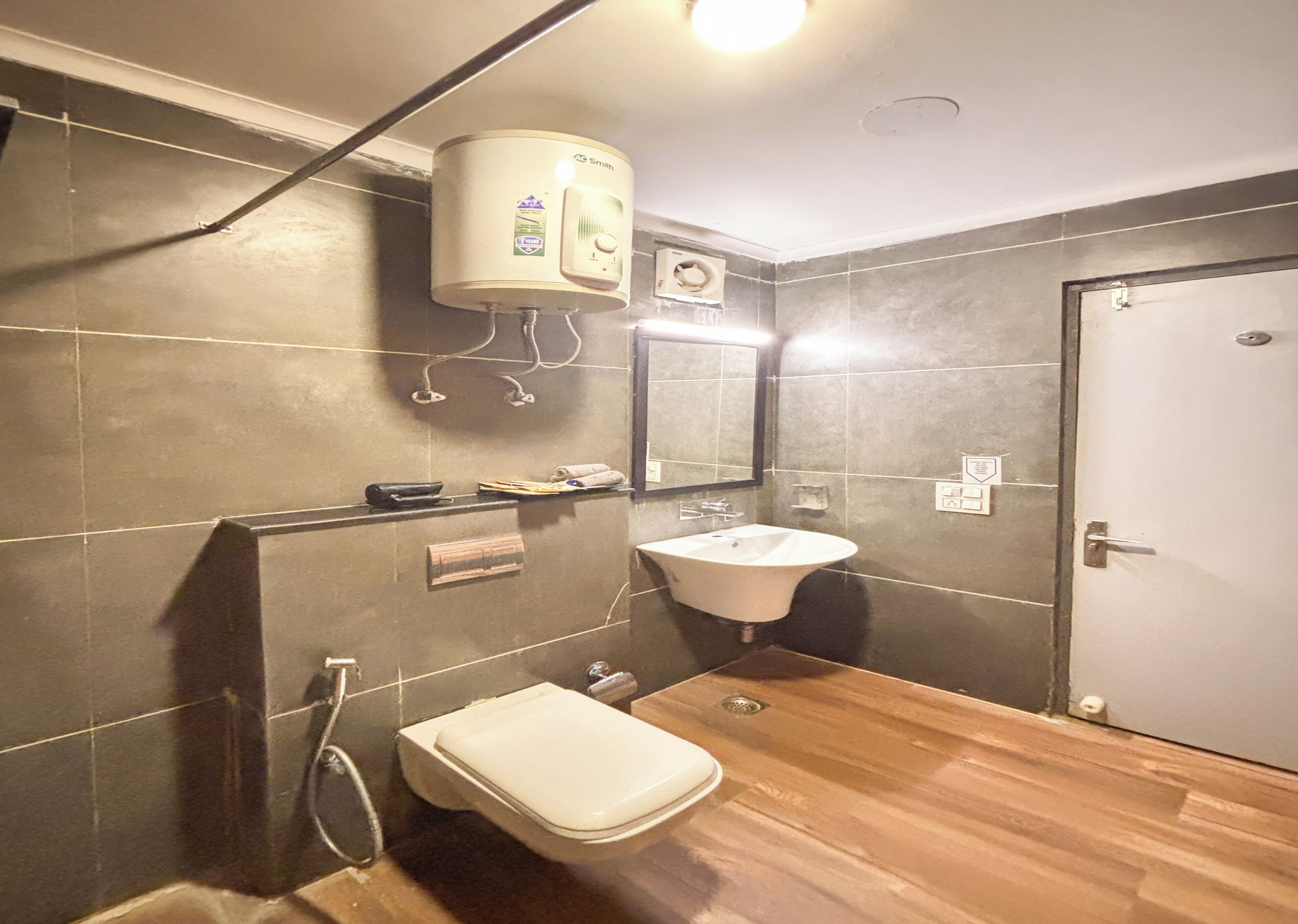 Un baño con inodoro, lavamanos y calentador de agua instalado en la pared.