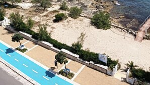 A coastal hotel with a beach view, a swimming pool, and a rocky shoreline.