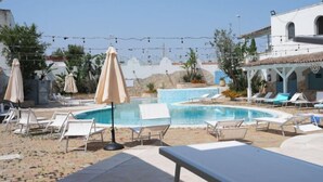 A pool area with lounge chairs and umbrellas, surrounded by buildings and plants.