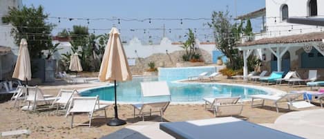 A pool area with lounge chairs and umbrellas, surrounded by buildings and plants.
