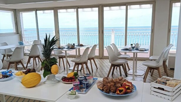 A dining area with tables set for breakfast, overlooking a balcony with a view of the sea.
