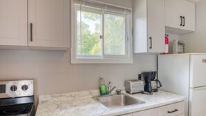 Eine Küche mit weißen Schränken, einer Edelstahl-Spüle, einem Herd, einem Fenster und einem Kühlschrank.