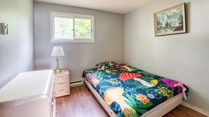 Ein Schlafzimmer mit Bett, Nachttisch, Lampe, Fenster und einem Bild an der Wand.
