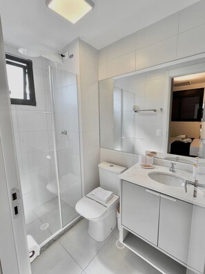 A modern bathroom with a glass-enclosed shower, a toilet, and a vanity with a sink and mirror. - Innvista - VibePinheiros (São Paulo)