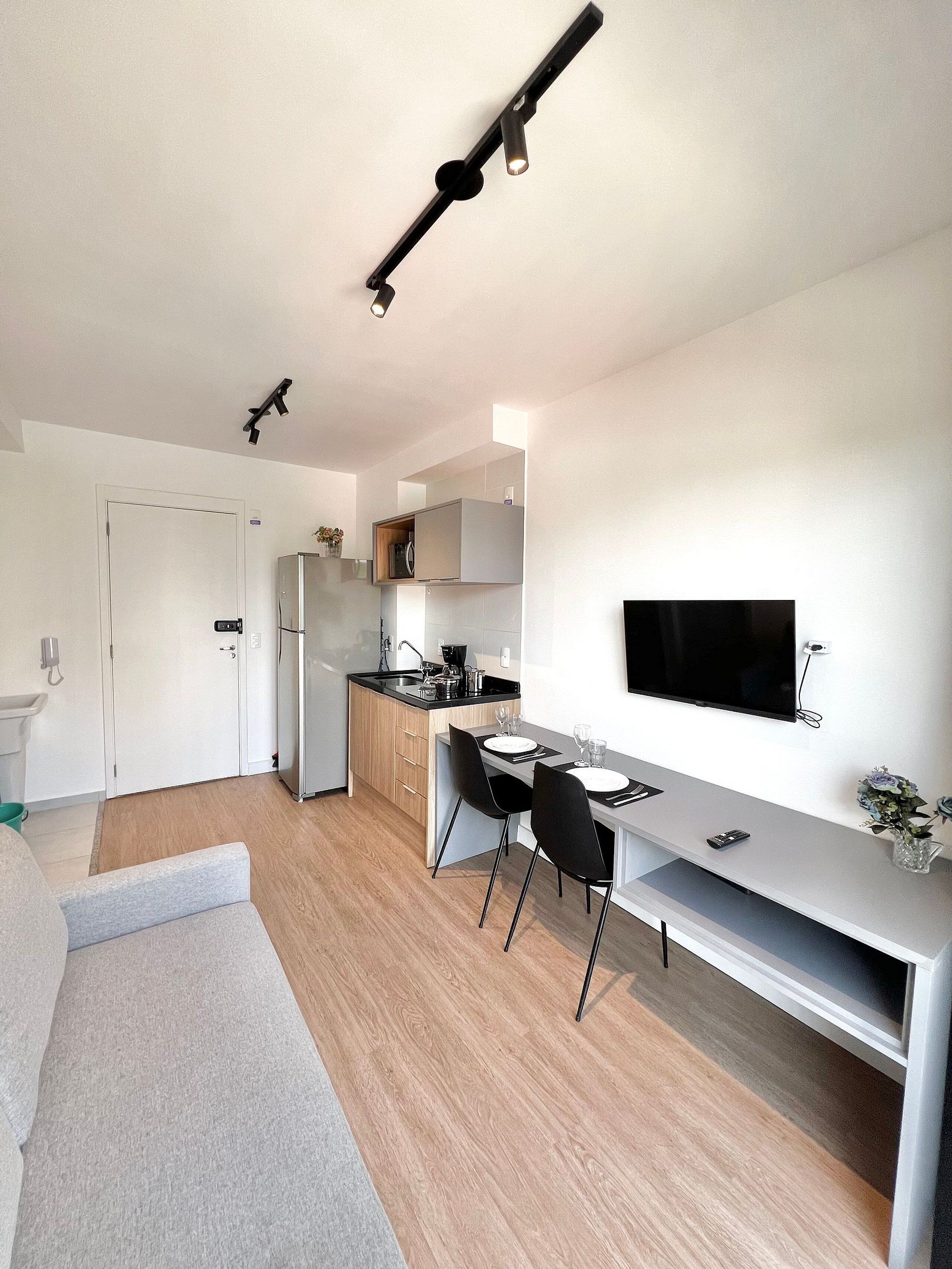 A modern kitchen with a dining area, a TV mounted on the wall, and a small seating area with a sofa.