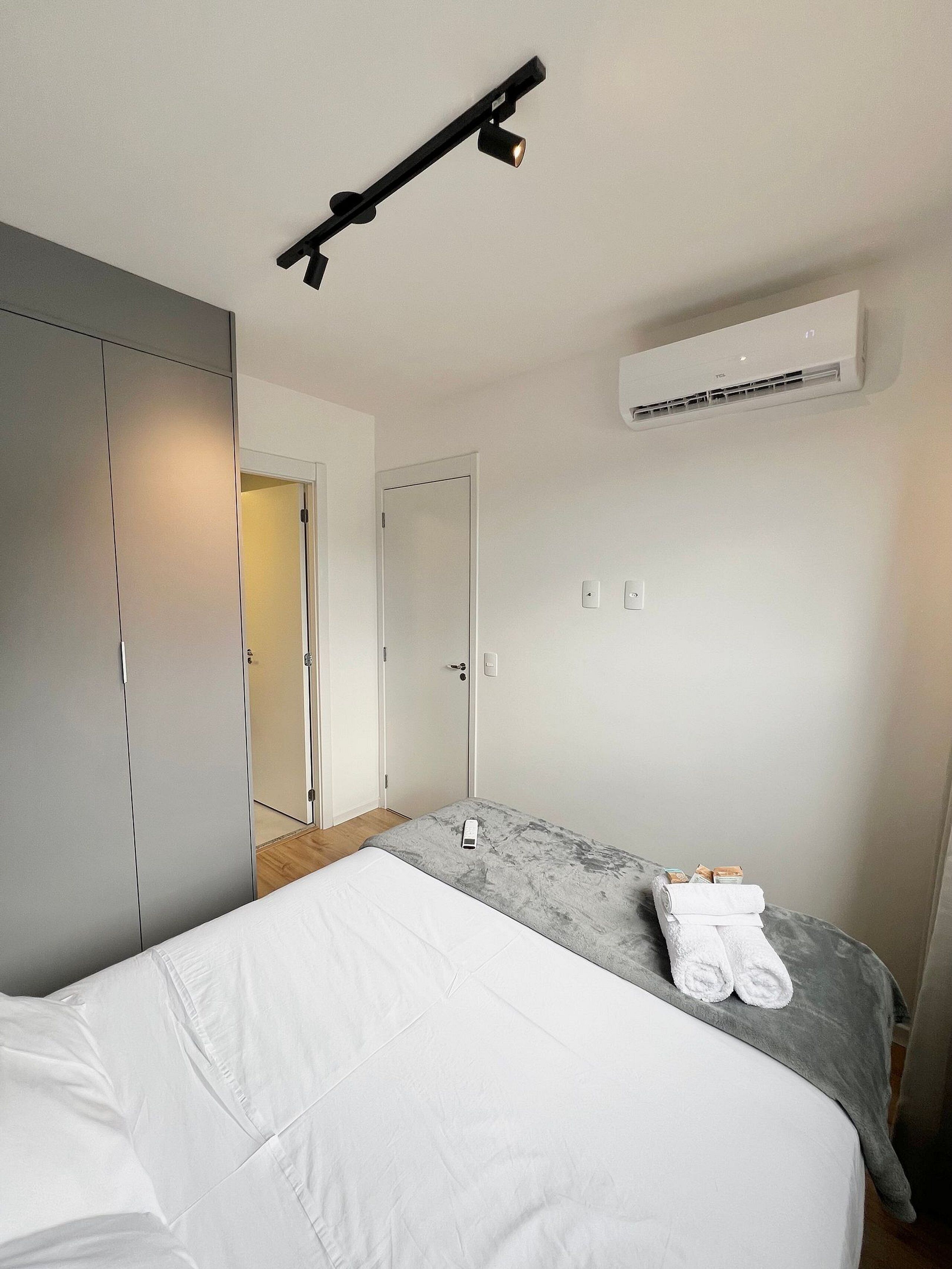 Een slaapkamer met een bed, een kledingkast, een airconditioning en een deur naar een andere kamer.