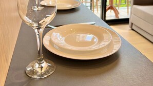 Une table à manger avec deux assiettes et deux verres à vin, un canapé et une vue sur les bâtiments à travers une grande fenêtre.