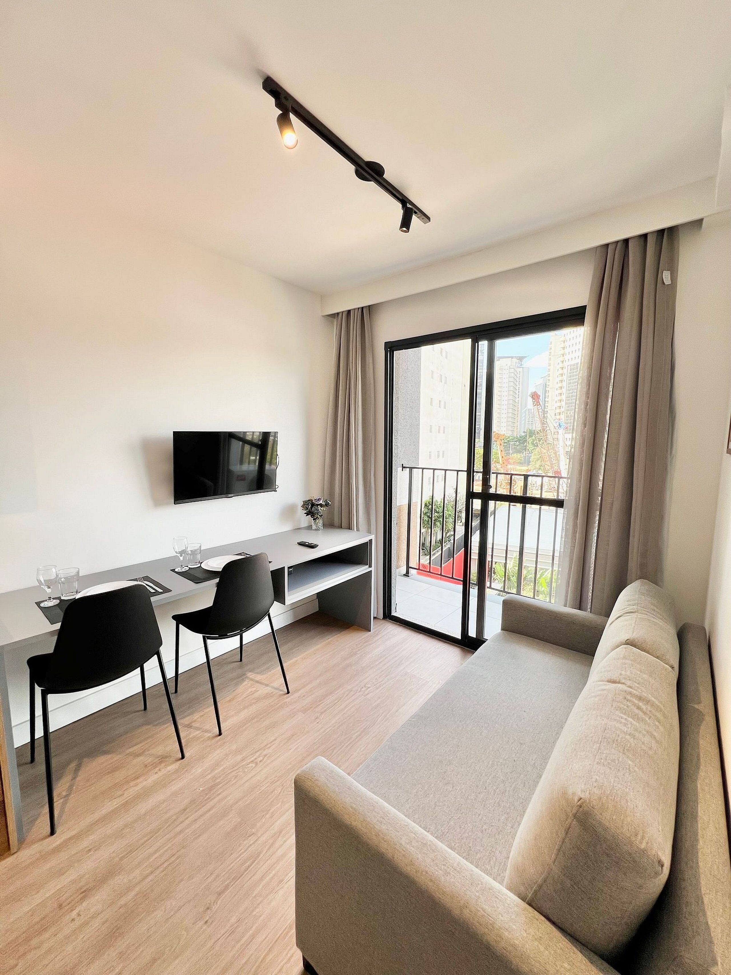 Un salon moderne comprenant un canapé, une table à manger avec des chaises, un téléviseur à écran plat fixé au mur et un balcon offrant une vue sur la ville.