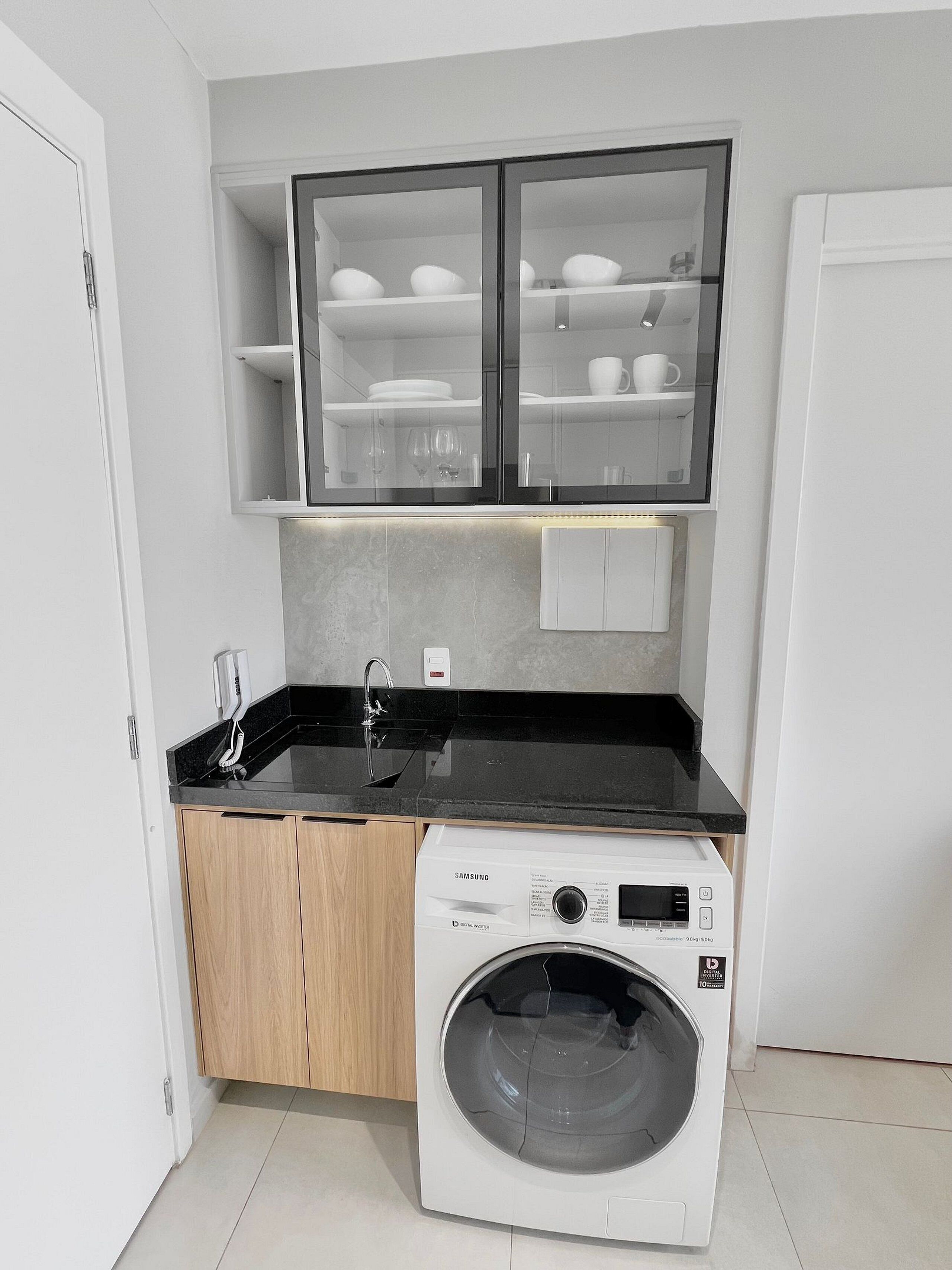 A compact kitchen with a built-in washing machine, a black countertop, and a cabinet with glass doors.