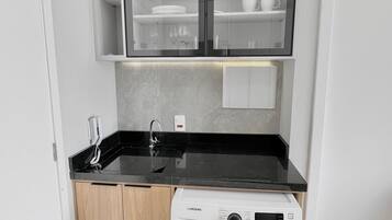 A compact kitchen with a built-in washing machine, a black countertop, and a cabinet with glass doors.