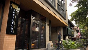 A building with a large glass entrance, a sign reading "ROSANEGRA APARTMENTS," and a person walking in front. - Warm Retreat at Rosa Negra Stadio (Medellín)