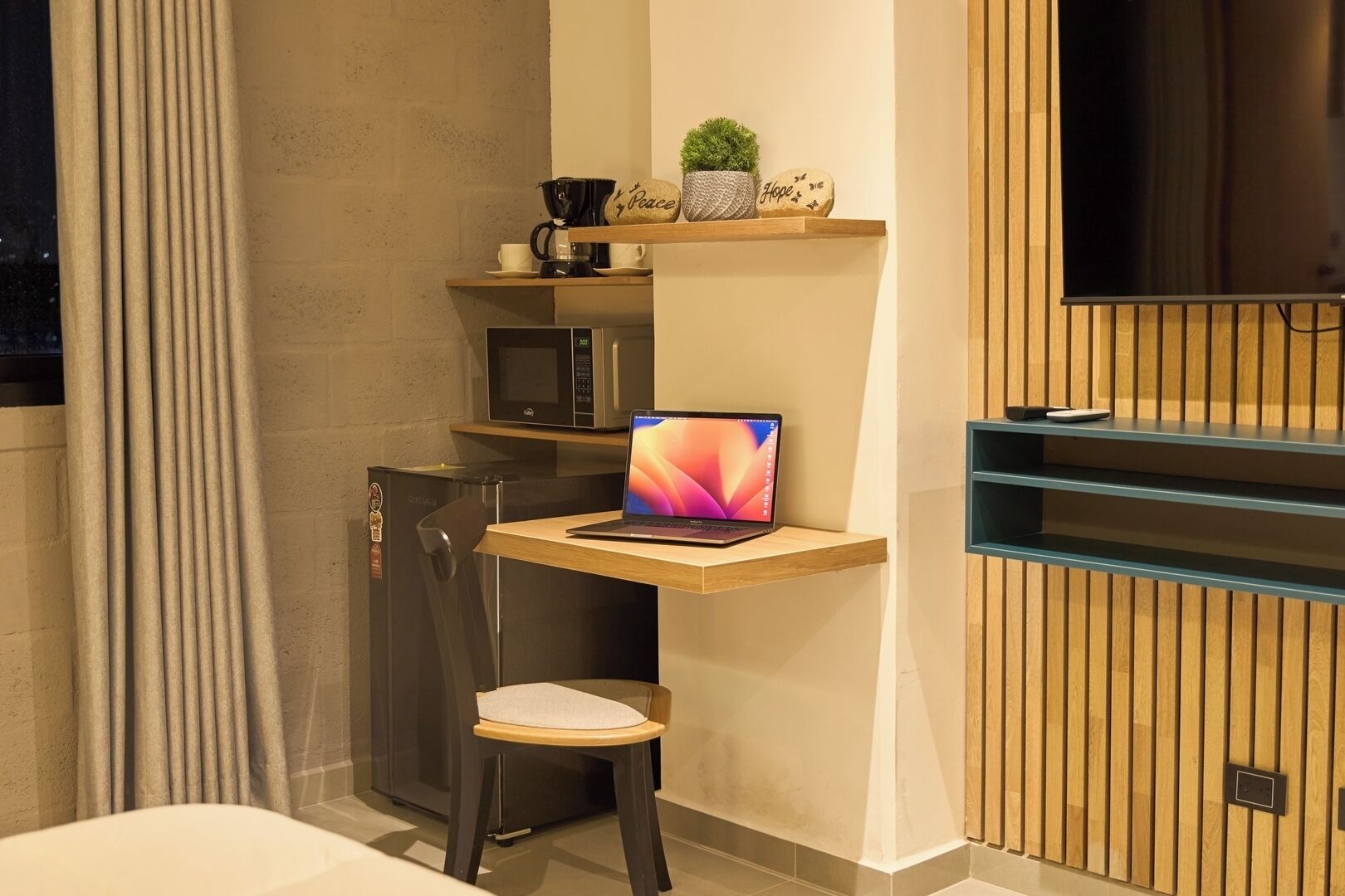 Un bagno moderno e compatto con doccia integrata, una piccola scrivania con un portatile, un forno a microonde e uno scaffale con oggetti decorativi.