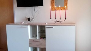 Una habitación moderna con un armario blanco, un televisor de pantalla plana en la pared, un espejo decorativo con marco dorado y un candelabro con velas.