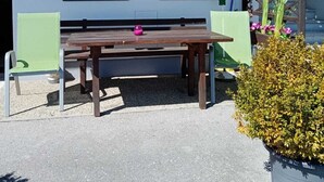 Un patio con una mesa de madera y dos sillas, una planta en maceta y una ventana con cortina.