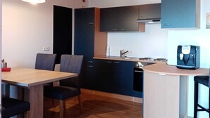 Una cocina compacta con armarios oscuros, techo de madera y un pequeño comedor con mesa y sillas.