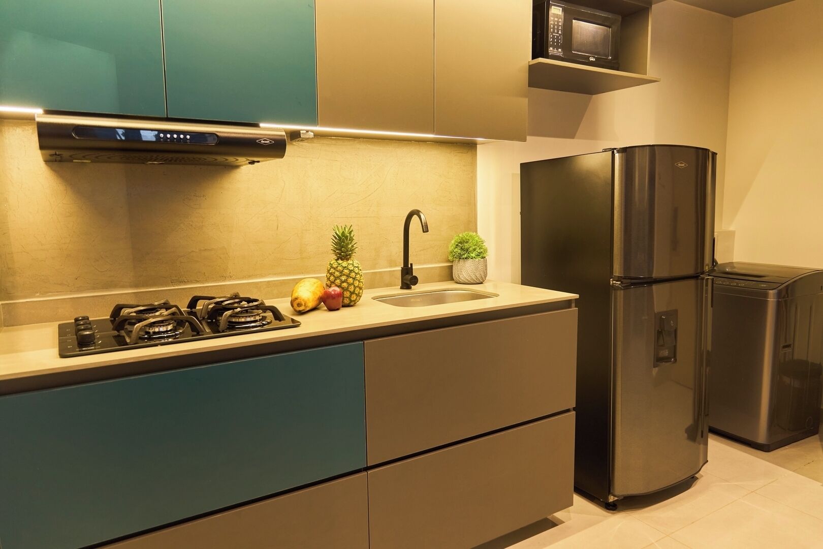 Una cocina moderna con armarios verde azulado y color crema, un refrigerador de acero inoxidable y un microondas sobre la estufa.