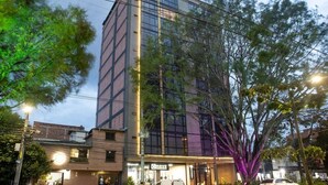 A modern building with a glass facade, a ground-level entrance, and a visible sign for a business. - Cozy Stadio Escape Rosa Negra Stay (Medellín)
