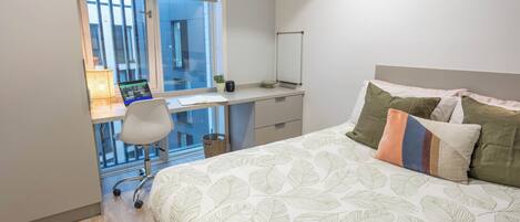 A bedroom with a bed, a desk, and a chair.
