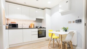 A modern kitchen with white cabinets, a microwave, an oven, and a dining table with yellow chairs. - City HideAway (Galway)