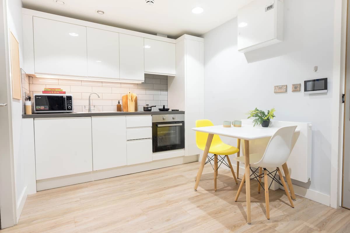 Cocina moderna con armarios blancos, microondas, horno y una mesa de comedor con sillas amarillas.