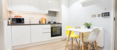 Cocina moderna con armarios blancos, microondas, horno y una mesa de comedor con sillas amarillas.