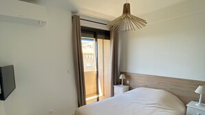 A bedroom with a large bed, a bedside table with a lamp, a small stool, and a TV mounted on the wall. - Ajaccio center ville magnifique appartement neuf vue mer 5p plage wifi parking (Ajaccio)