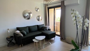 A modern living room with a black sectional sofa, a small white table, and a wooden dining table. There are three round mirrors on the wall, a ceiling fan, and a potted orchid plant. - Ajaccio center ville magnifique appartement neuf vue mer 5p plage wifi parking (Ajaccio)
