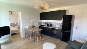 A modern living room with a green sofa, a dining area with a table and chairs, a kitchen with black cabinets and a black refrigerator, and a TV in the corner. - Ajaccio center ville magnifique appartement neuf vue mer 5p plage wifi parking (Ajaccio)