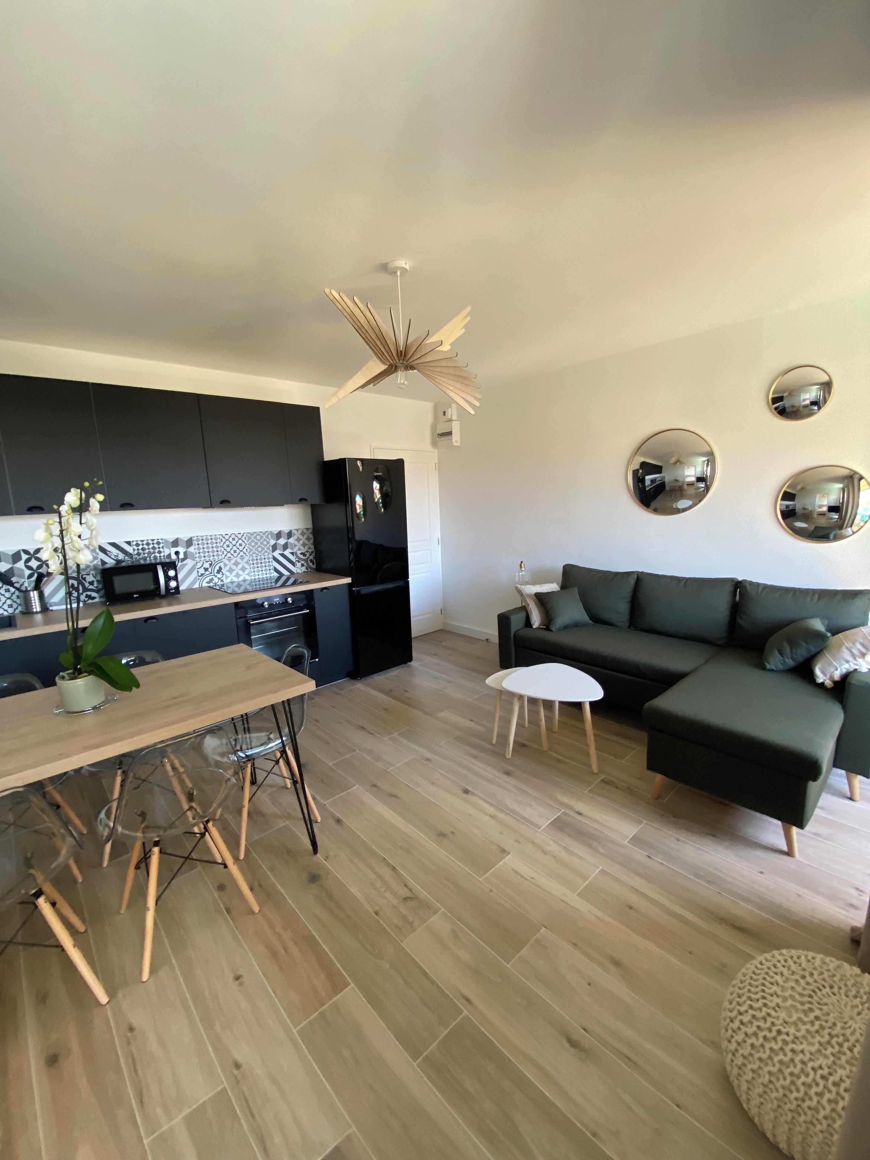 A modern kitchen with dark cabinets, a black refrigerator, and a wooden dining table with chairs.
