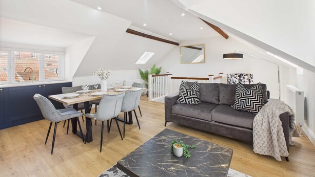 A modern loft apartment with a dining area, a sofa with patterned cushions, and a marble coffee table. - Host Stay Admiral s View (Whitby)