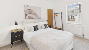 A bedroom with a large bed, a nightstand with drawers, a wall-mounted artwork, a window with a view of buildings, and a radiator. - Host Stay Admiral s View (Whitby)