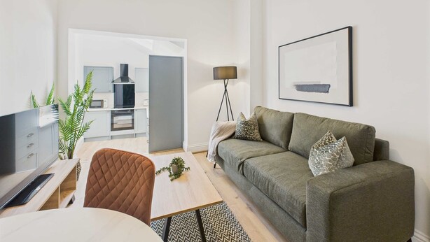 A modern living room with a sofa, a coffee table, and a TV. There is a kitchen area in the background with a microwave and a stove. - Host Stay Captain s View (Whitby)