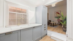 A modern kitchen with grey cabinets, a white countertop, and a window with blinds. - Host Stay Captain s View (Whitby)