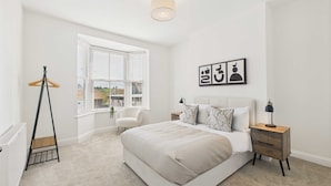 A bedroom with a large bed, a bedside table with a lamp, a chair, and a window with blinds. - Host Stay Captain s View (Whitby)