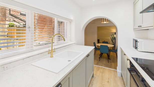 A modern kitchen with a large window, white cabinetry, and a dining area visible through an archway. - Host Stay Holmwood (Whitby)