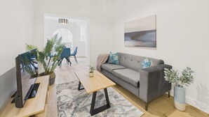 A modern living room with a grey sofa, a wooden coffee table, a TV on a stand, and a potted plant. - Host Stay Holmwood (Whitby)