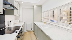 A modern kitchen with a built-in stove, a sink, and a window with blinds. - Host Stay Holmwood (Whitby)