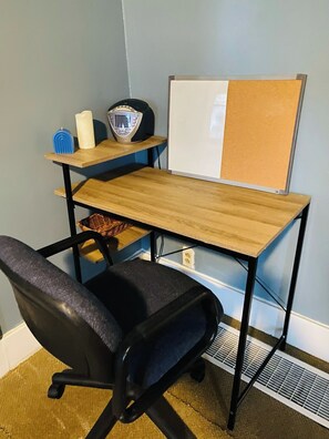 A desk with a computer, a chair, a whiteboard, and a shelf with a speaker and a candle.