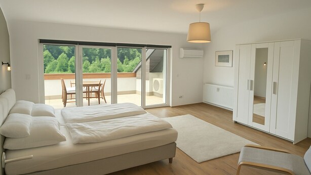 A bedroom with a bed, a chair, a wardrobe, and a view of a balcony with a table and chairs. - Neckar View Apartment near Heidelberg | Balcony & Parking (Neckarsteinach)