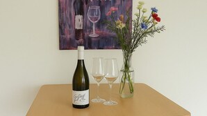 A wooden table with a wine bottle and two glasses on it, a vase with flowers, and a painting on the wall. - Neckar View Apartment near Heidelberg | Balcony & Parking (Neckarsteinach)