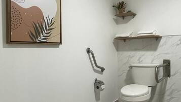 A modern bathroom with a toilet, grab bars, a towel rack, and a framed artwork on the wall.