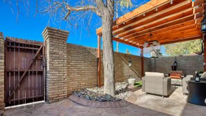 A patio area with a pergola, outdoor furniture, a brick wall, and a wooden gate. - Charming Oasis Apartment (El Paso)