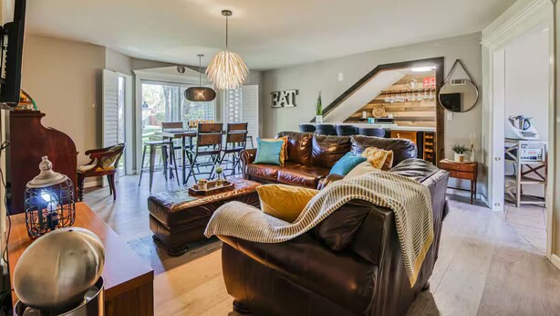 A spacious living room with a leather sofa, a dining area with chairs, a kitchen in the background, and a staircase leading to another level. - Charming Oasis Apartment (El Paso)